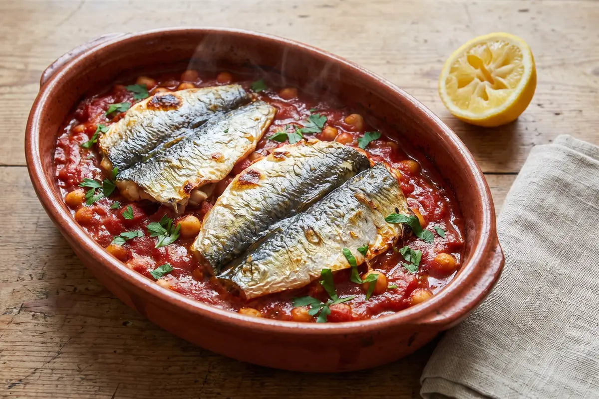 Baked butterflied sardines on a tomato and chickpea sauce in an oval dish with parsley
