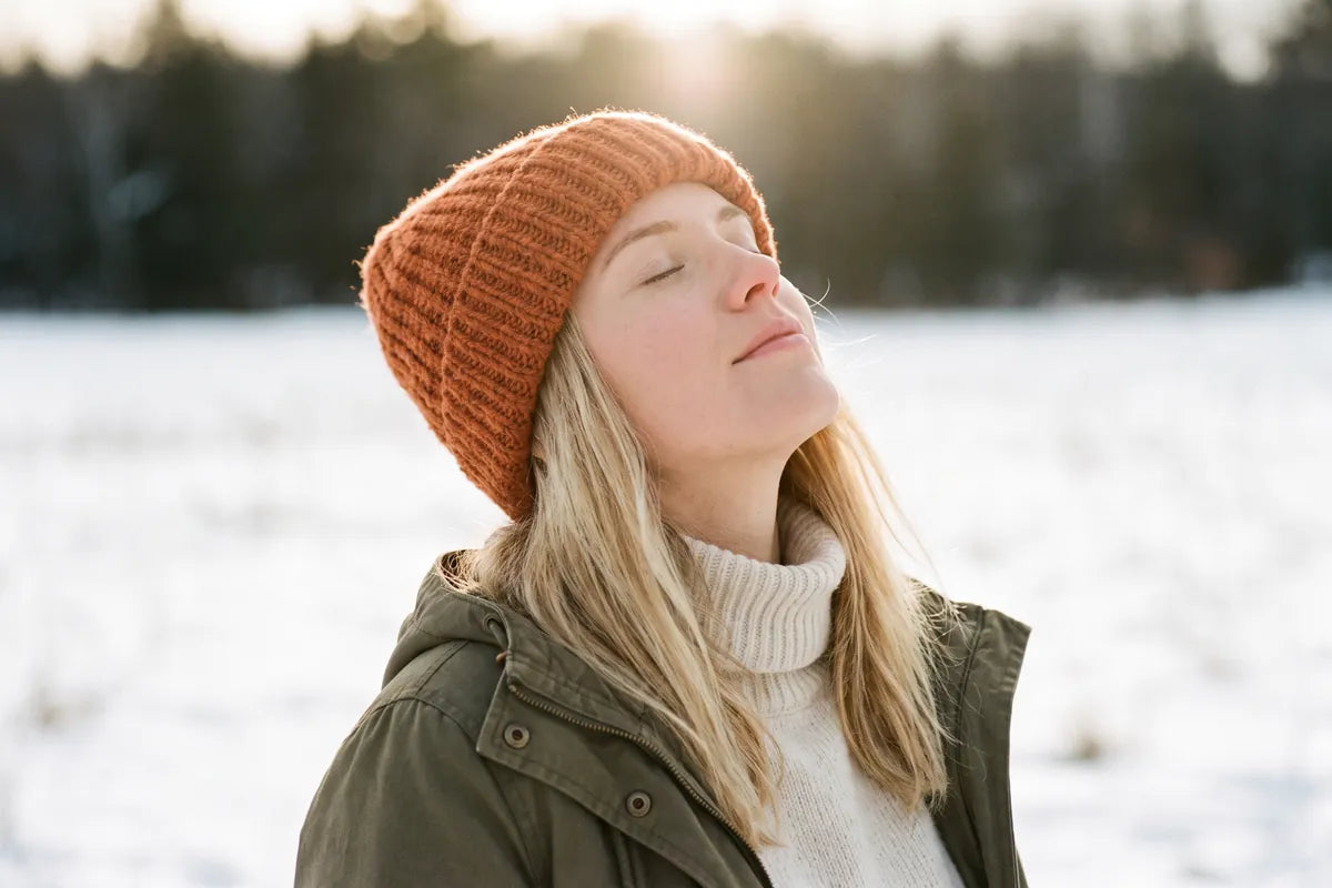 Portrait of a woman with eyes closed, face tilted up into winter sunlight, backlit against a snowy field