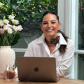Woman sitting at a table with a laptop, smiling outdoors.