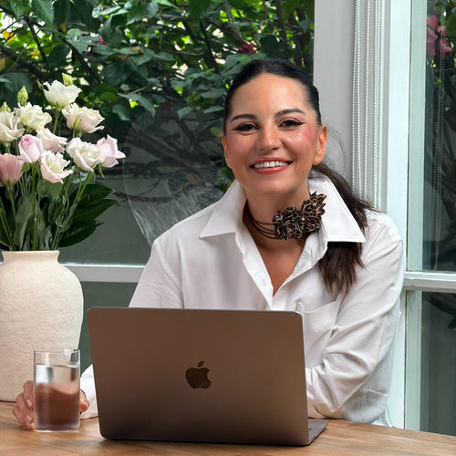 Woman sitting at a table with a laptop, smiling outdoors.