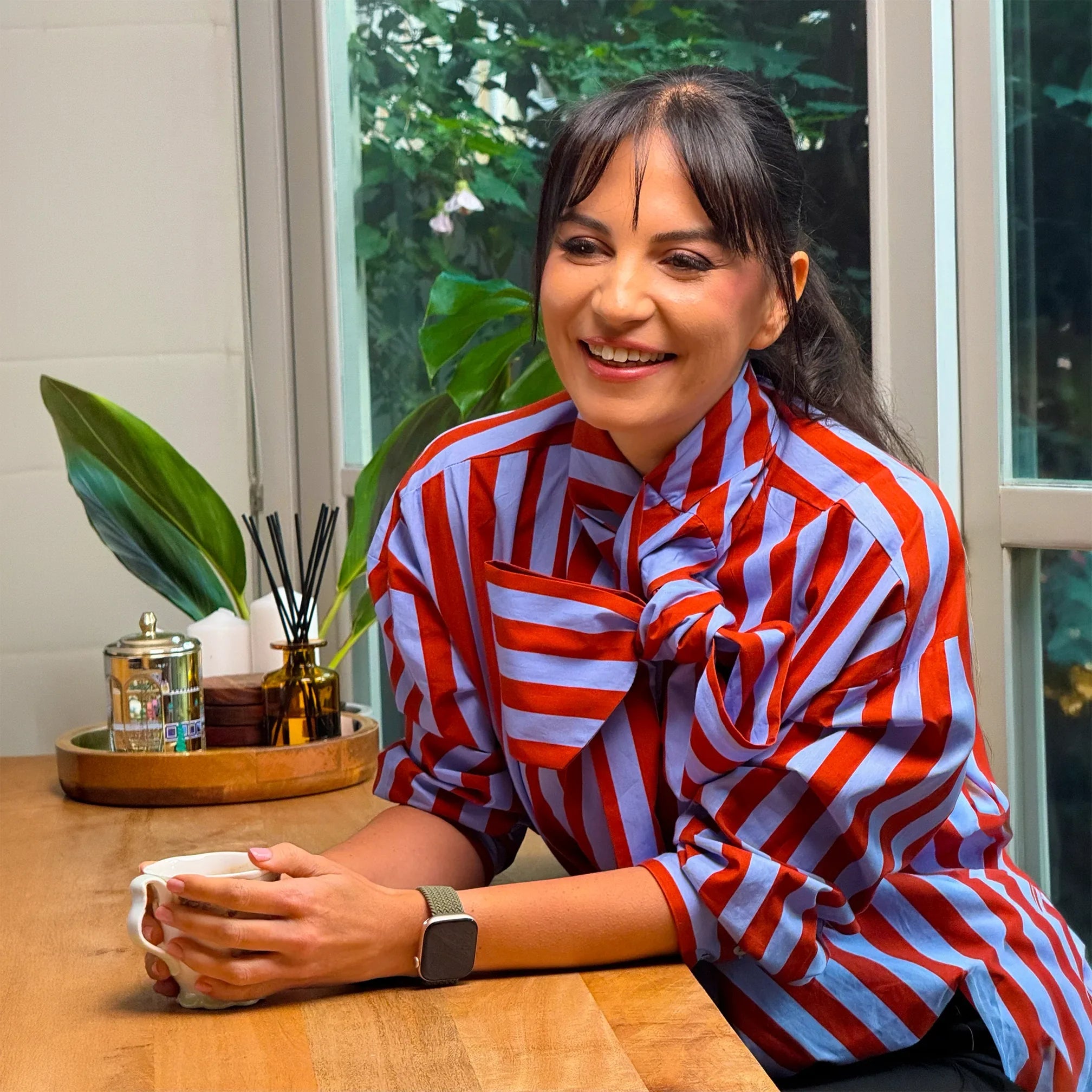 MSc Dietitian Merve Tigli smiling at a table with a cup of tea, wearing a red and blue striped shirt.